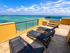 A balcony with two sun loungers and a small table, overlooking a clear blue sea with a pier in the distance. - Luxury Oceanfront 3BR Condo with Huge Terrace, Private Plunge Pool & Ocean Views (Playa del Carmen)