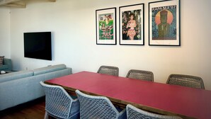 A conference room with a long table, wicker chairs, a flat-screen TV, and three framed posters on the wall. - Zeni House (Otaru City)