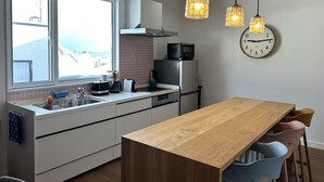A modern kitchen with a wooden table, white cabinets, a microwave, and a clock on the wall. - Zeni House (Otaru City)