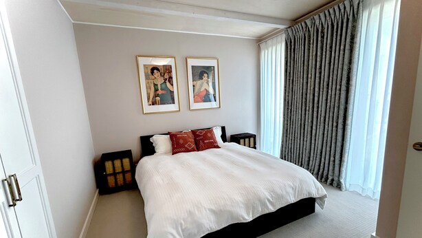 A bedroom with a large bed, two framed pictures on the wall, a window with curtains, and a door. - Zeni House (Otaru City)