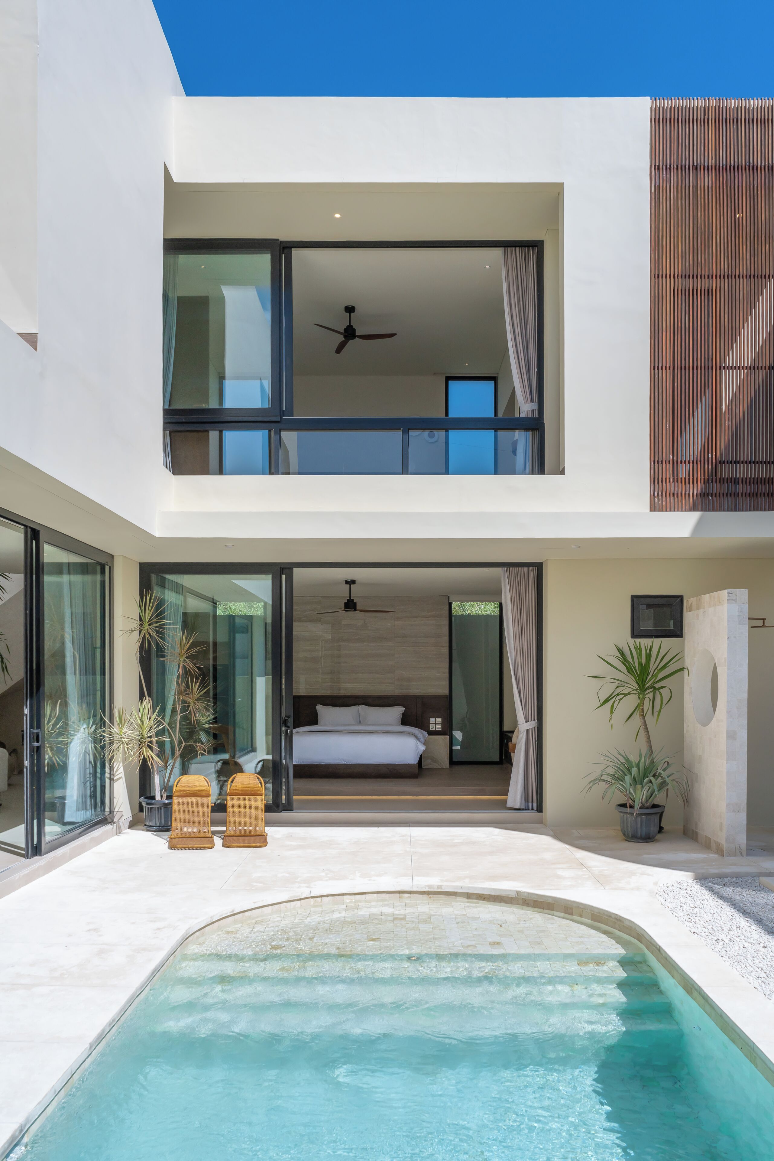 A modern two-story building with a swimming pool, a balcony with a bed, and a ceiling fan.