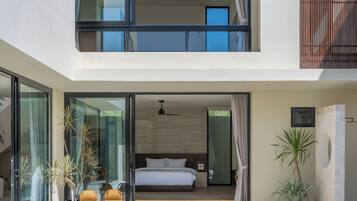 A modern two-story building with a swimming pool, a balcony with a bed, and a ceiling fan.