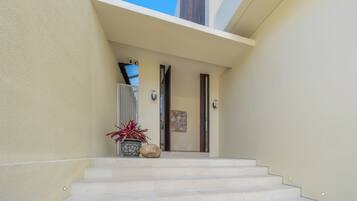 A modern building entrance with a set of stairs leading to a door, a potted plant, and a security camera.