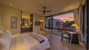 A modern hotel room with a large bed, a desk with a chair, and a balcony with a view of the sunset. - NAVA - Contemporary 3BR Villa (Badung)