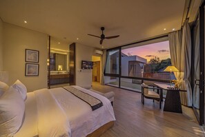 Ein modernes Hotelzimmer mit einem großen Bett, einem Schreibtisch mit Stuhl und einem Balkon mit Sonnenuntergangsblick.