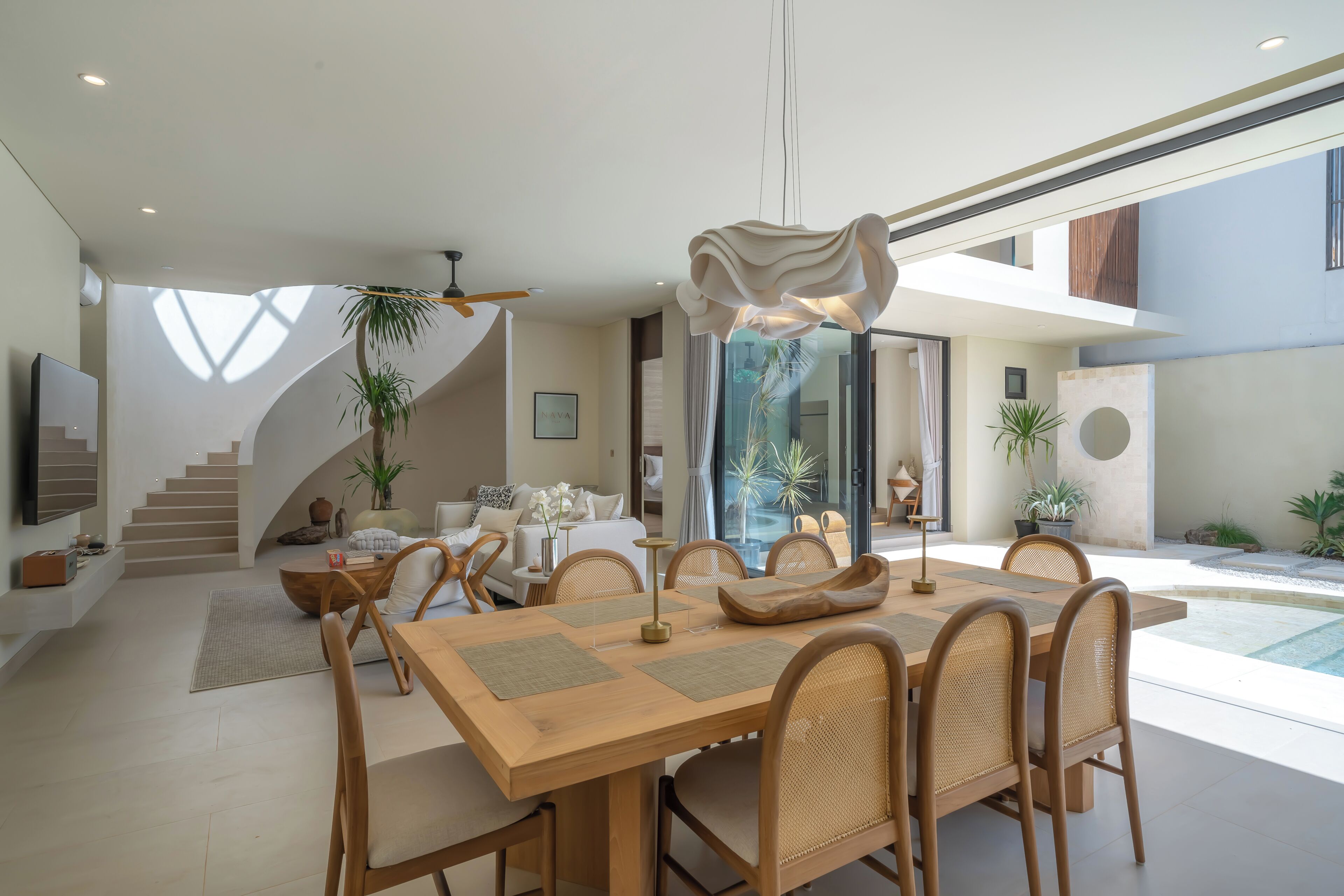 A modern interior with a dining area, staircase, and outdoor space with plants.