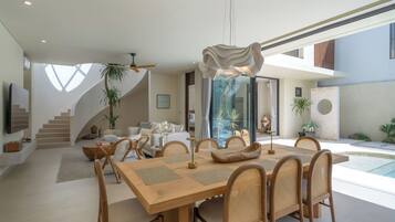 A modern interior with a dining area, staircase, and outdoor space with plants.