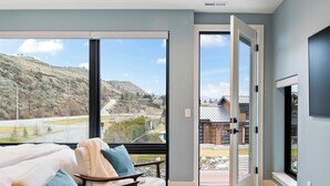 A modern living room with a sofa, a rug, and a view of a mountainous landscape through large windows.