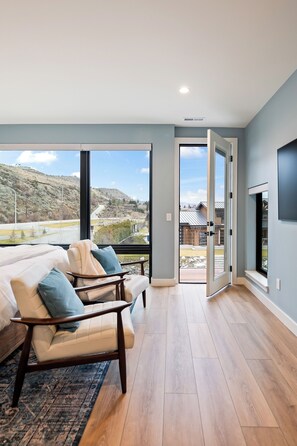 A modern living room with a sofa, a rug, and a view of a mountainous landscape through large windows.