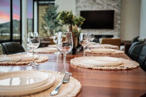 A dining table set with plates, glasses, and cutlery, with a TV and plants in the background.