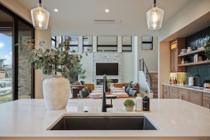 A modern kitchen with a large island, a built-in stove, and a sink. There is a dining area with a large table and chairs, and a living room with a fireplace and a TV.