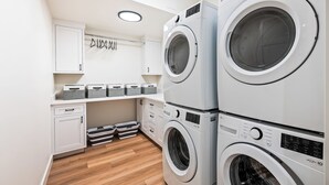 A laundry room with stacked front-loading washing machines, a drying rack, and storage bins.
