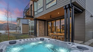 A modern house with a hot tub in the backyard, a dining area, and a view of the mountains.