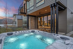 A modern house with a hot tub in the backyard, a dining area, and a view of the mountains.