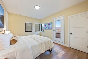 A bedroom with a bed, a door, a window, and a wall-mounted picture.