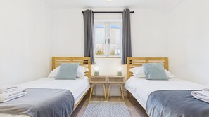 Habitación doble con dos camas, una ventana con cortinas, mesitas de noche con lámparas y una alfombra estampada.