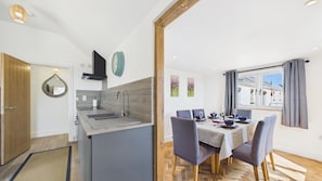 Eine moderne Küche mit integrierter Kochinsel, einem Essbereich mit Tisch für zwei Personen und einem großen Fenster mit Vorhängen.