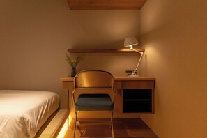 Habitació compacta amb un llit, una taula de treball amb una cadira i una làmpada de taula.
