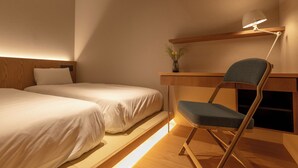 Et hotelværelse med to senge, et skrivebord, en stol, en lampe og en vase med blomster.