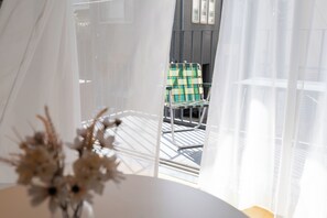 A room with a view of a balcony, a chair, and a table with a vase of dried flowers. - ALMOND HOTEL SHIBUYA W (shibuya)