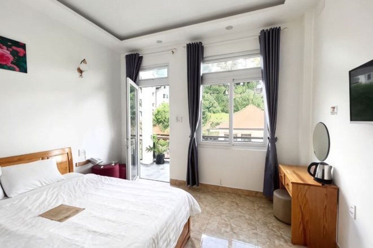 Habitación de hotel con cama, escritorio, espejo y vistas al exterior.