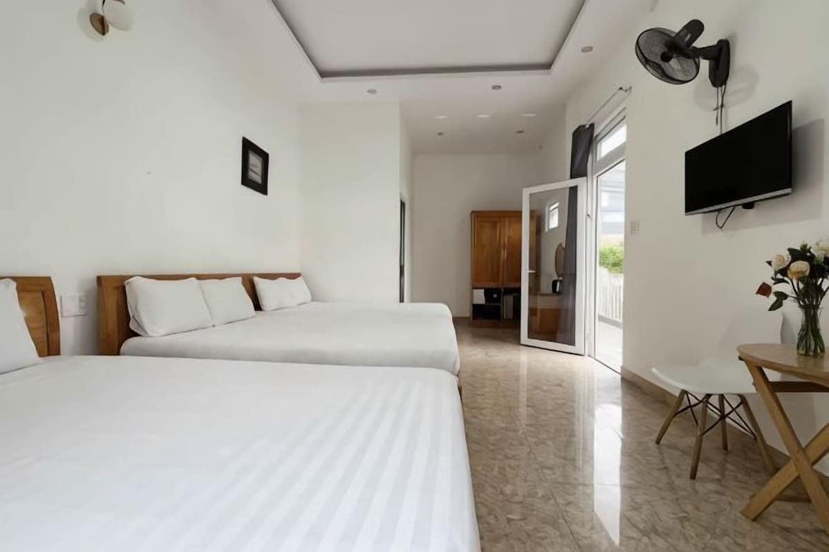 A hotel room with two beds, a TV, a desk, and a dining area.