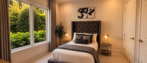 A bedroom with a large window, a ceiling fan, a bed with a dark headboard, and a bedside table with a candle.