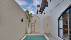 Un área de piscina moderna con una piscina azul cristalina, una planta en maceta y una escalera que lleva a una puerta.