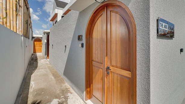 Un estrecho callejón con una puerta de madera y un cartel que indica 'The Ark Canggu'.