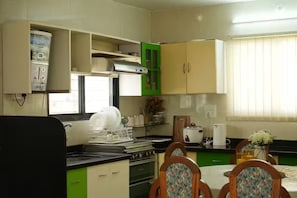 A compact kitchen with a stove, sink, and green cabinets. There is a dining table with chairs and a vase of flowers. - Vayavia White House / Where Comfort Feel Like Home (Nashik)