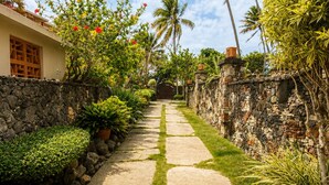 Un sendero que conduce a un edificio con un muro de piedra y plantas tropicales.