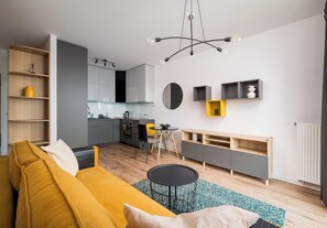 A modern living room with a yellow sofa, a round mirror, and a kitchen in the background. - Lotnisko Chopina Chic Apartment (Warszawa)