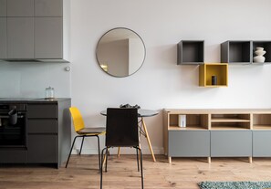 A modern kitchen with grey cabinets, a round mirror, a yellow chair, a round table, and a wooden floor. - Lotnisko Chopina Chic Apartment (Warszawa)