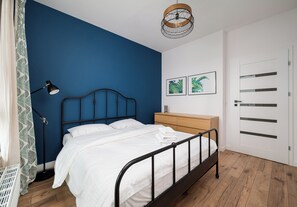 Een slaapkamer met een bed, een bedlamp, een houten dressoir, een deur en twee ingelijste foto's aan de muur.