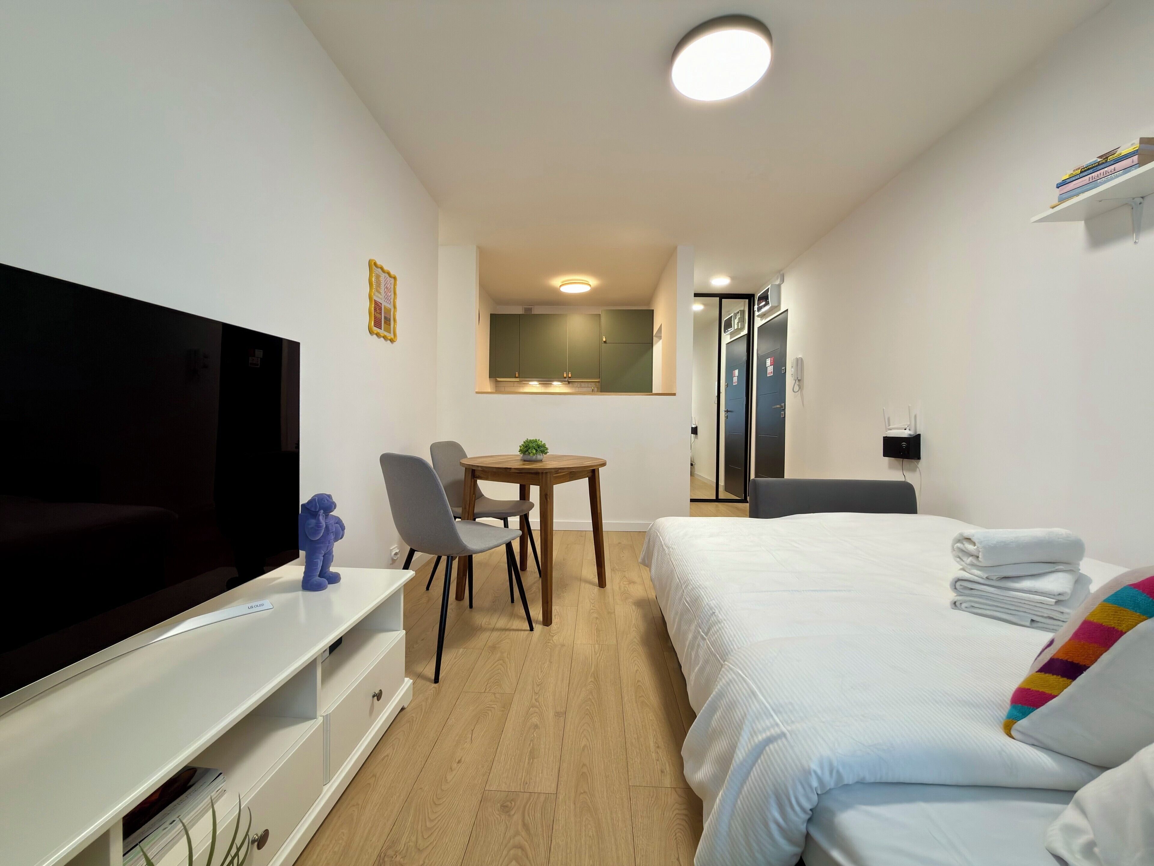 A hotel room with a bed, a TV, a desk with chairs, a small table, and a wardrobe.