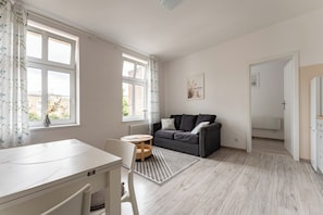 Ein modernes Wohnzimmer mit einer Couch, einem Esstisch und Blick durch große Fenster ins Freie.