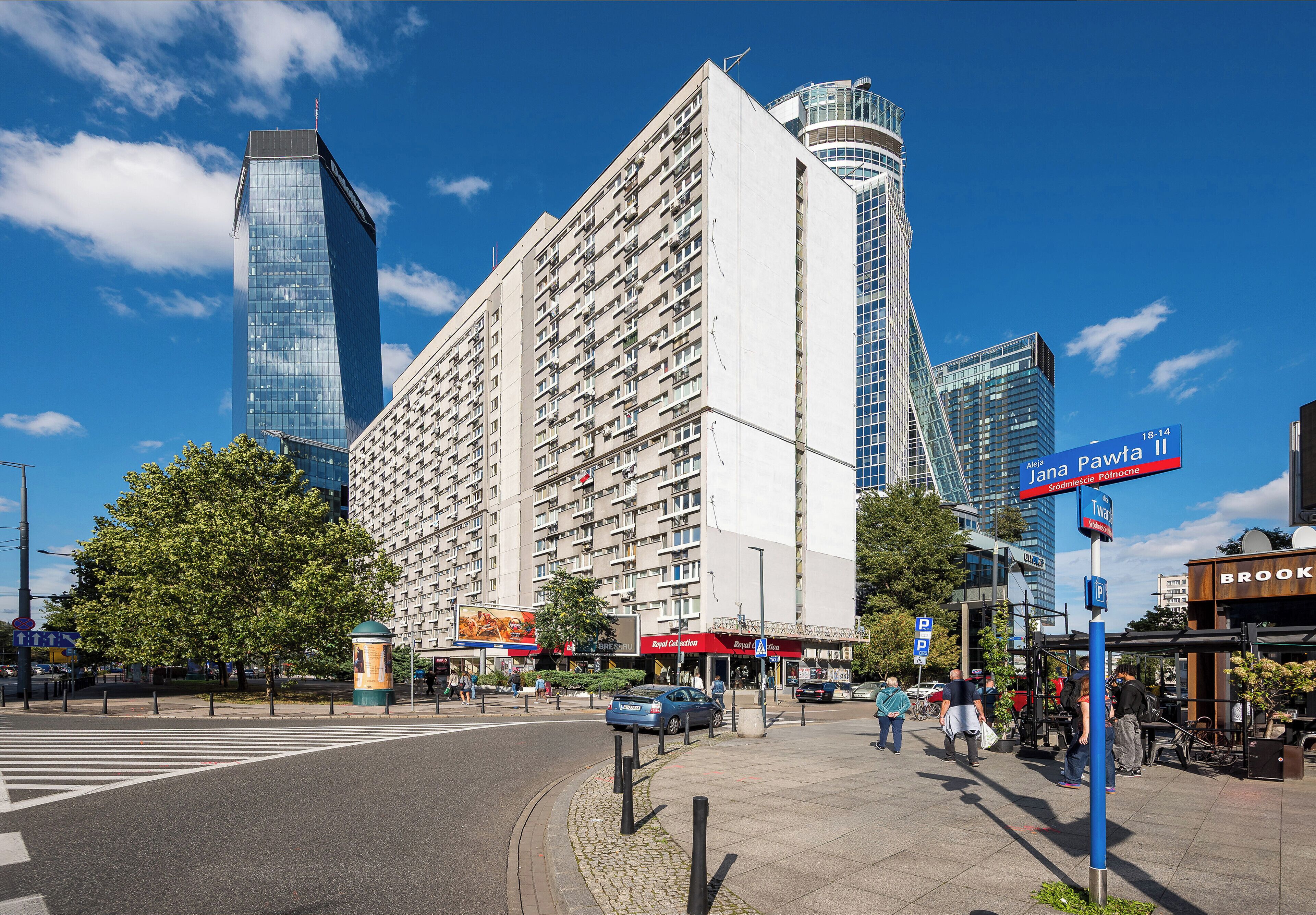 A city street with modern buildings, a pedestrian crossing, and a clear blue sky.