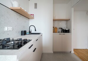 A modern kitchen with a gas stove, black faucet, and wooden shelves. - Rondo ONZ Cozy Stay Apartment (Warszawa)
