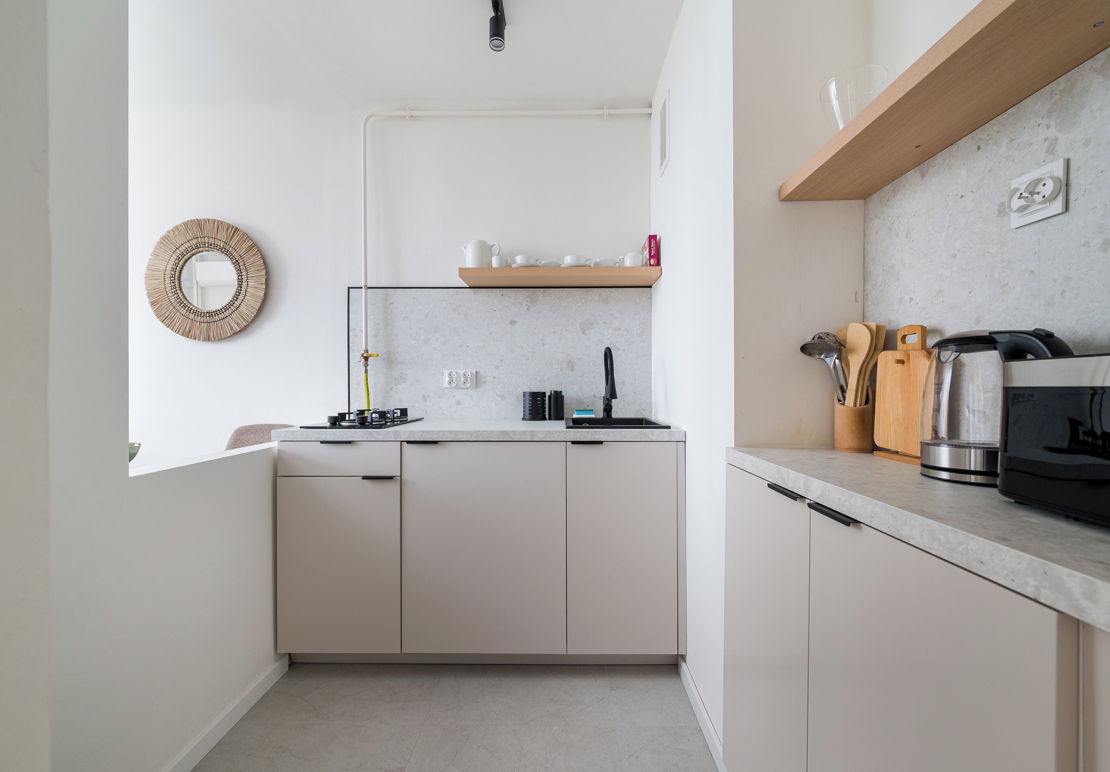 Cocina moderna con armarios blancos, lavavajillas integrado, cafetera y estante de madera con utensilios de cocina.
