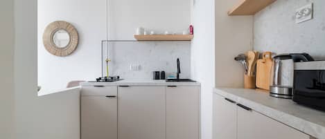 Cocina moderna con armarios blancos, lavavajillas integrado, cafetera y estante de madera con utensilios de cocina.