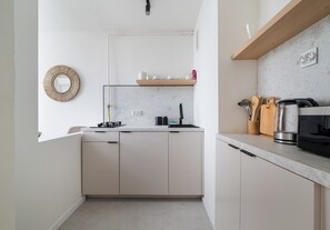 Eine moderne Küche mit weißen Schränken, einem eingebauten Geschirrspüler, einer Kaffeemaschine und einem Holzregal mit Küchenutensilien.