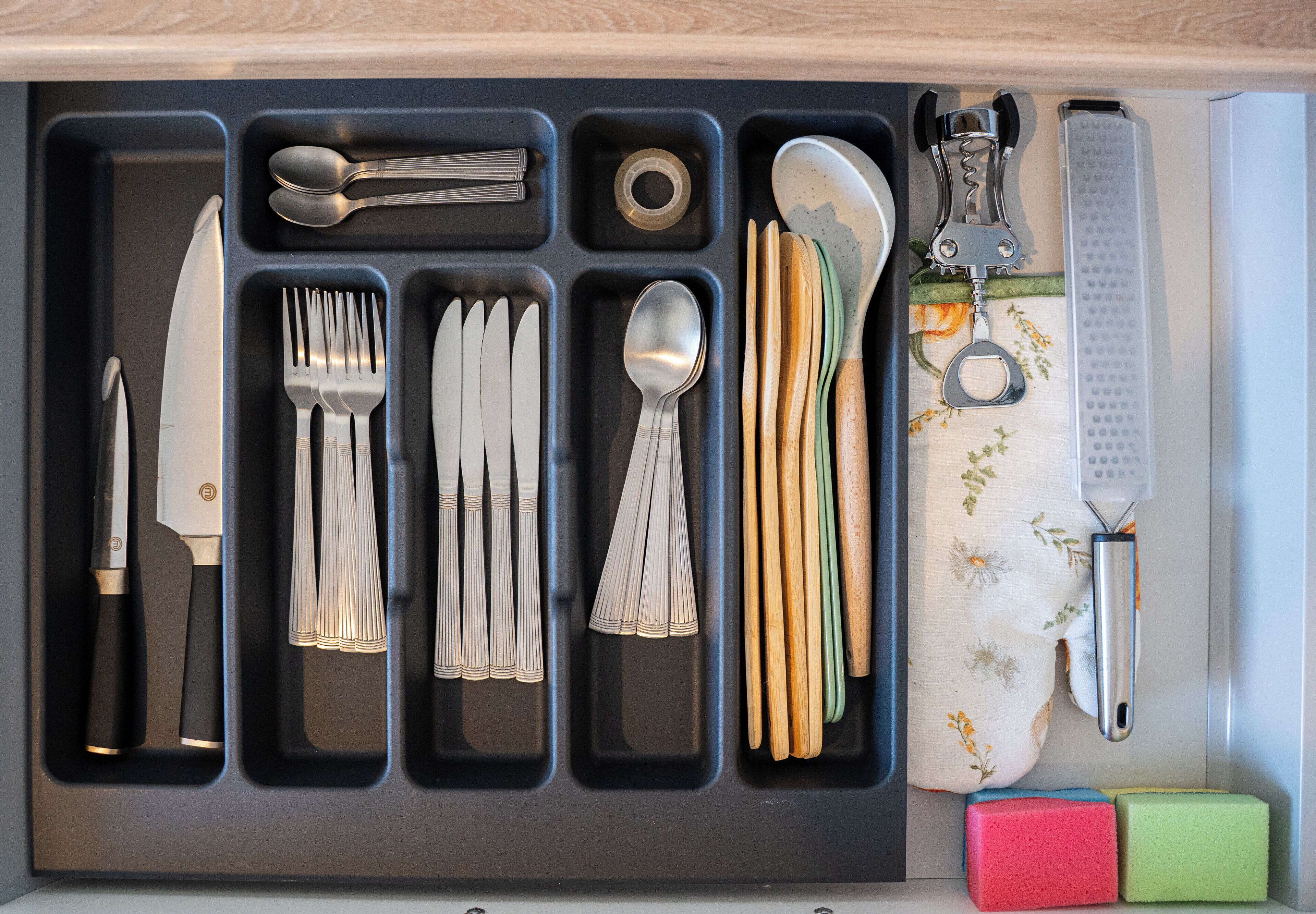 A drawer with utensils, including forks, knives, spoons, and a bottle opener.