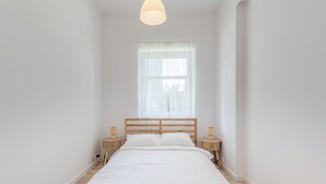 Un dormitorio con una cama individual, un ventanal con cortinas translúcidas y dos lámparas de noche.