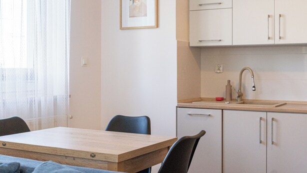 Una cocina con una mesa de madera, sillas, armarios y un lavamanos.