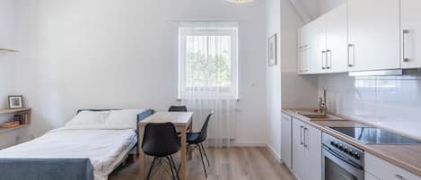 A compact, modern room with a bed, a dining table, and a kitchenette.