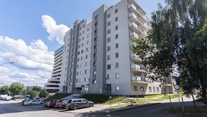 Un edificio residencial de varios pisos con balcones, un área de estacionamiento y un sendero para peatones.