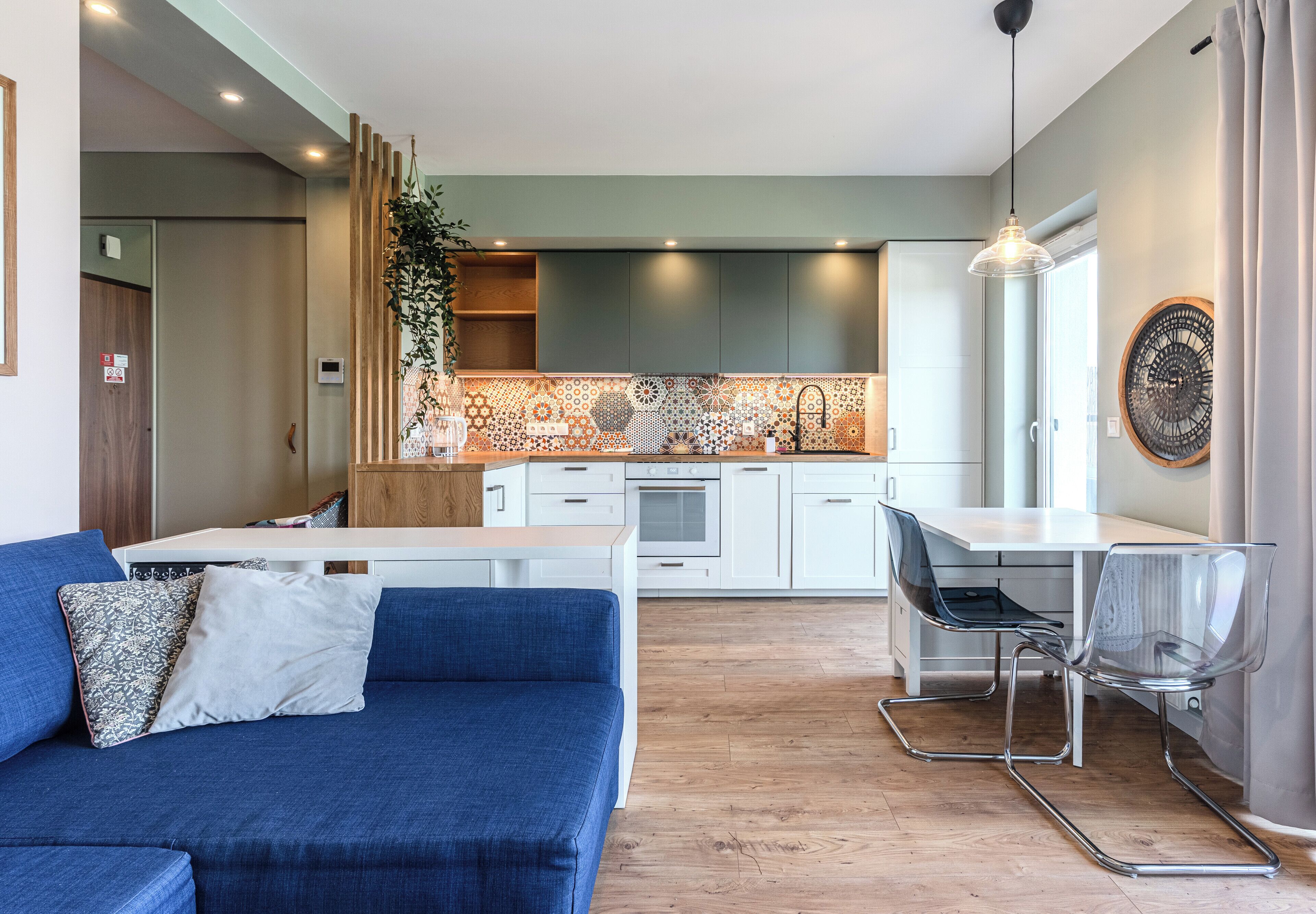 A modern kitchen with white cabinets, a patterned backsplash, and a dining area with a clear glass table and metal chairs.