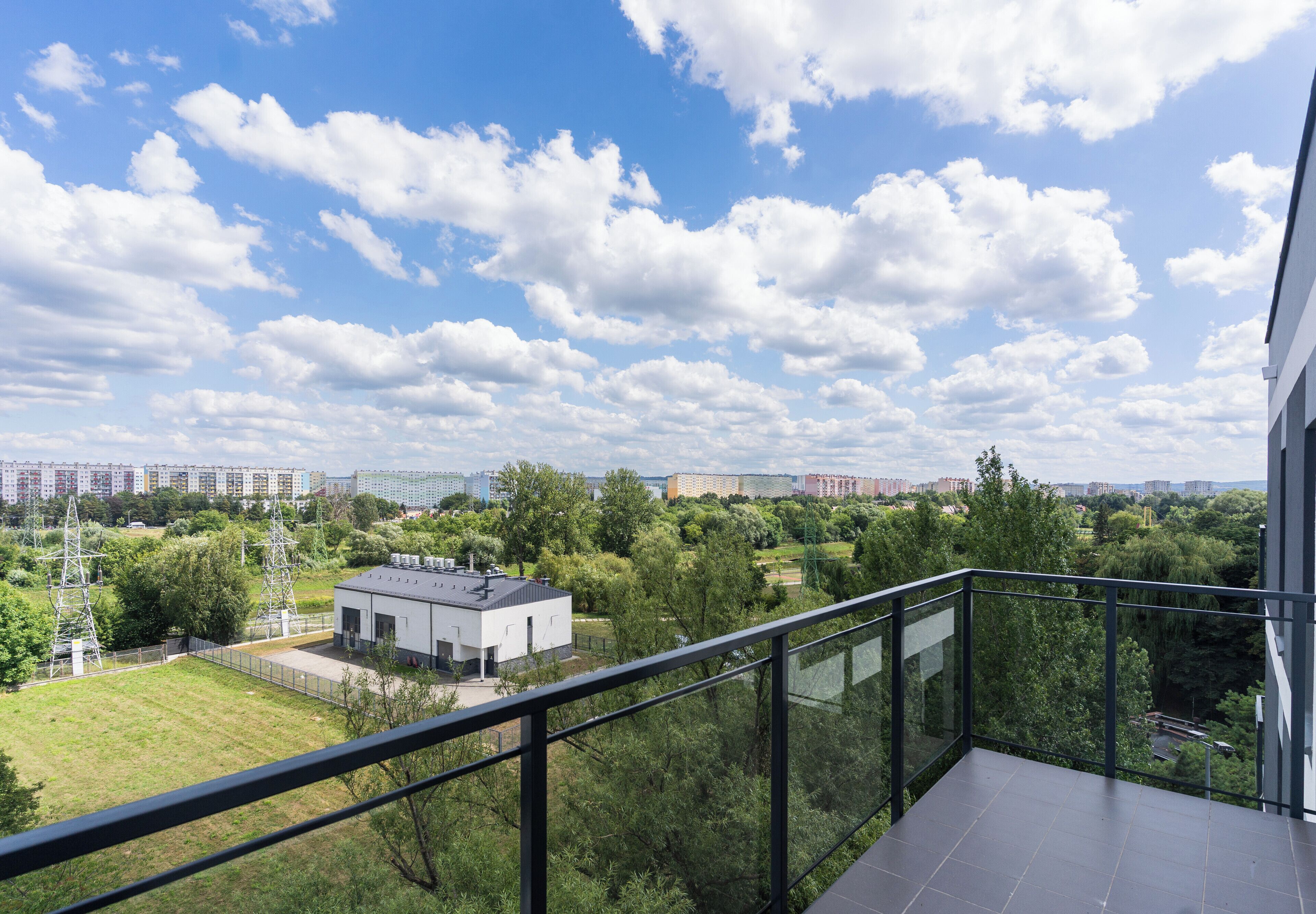 A balcony with a clear view of a cityscape, including residential buildings and greenery.