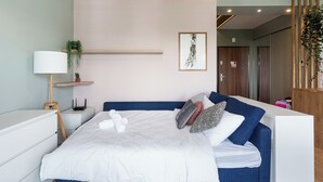 Ein modernes Schlafzimmer mit Bett, Nachttisch, Lampe und einer Wandablage mit Pflanzen.