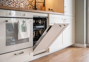 An open oven with a towel hanging on the handle, a dishwasher, and a wooden countertop with a patterned backsplash.